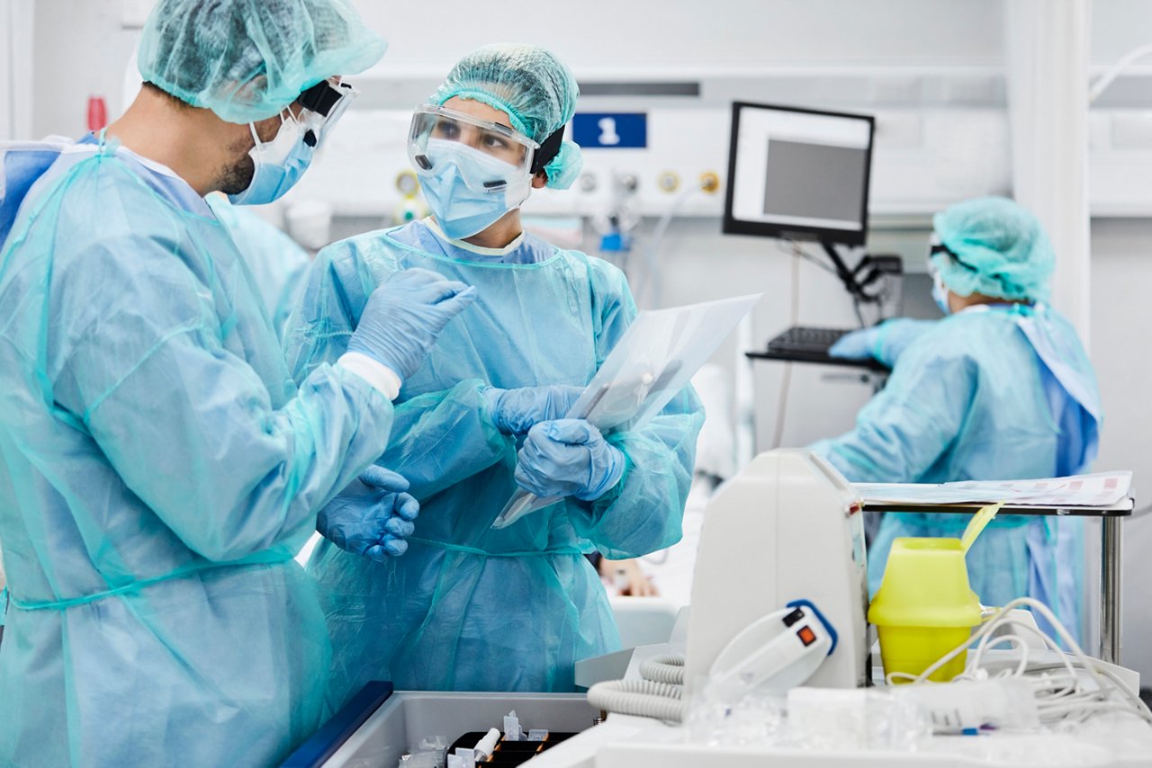 Male and female doctors discussing while standing in ICU. Healthcare workers are protective workwear. They are at hospital.