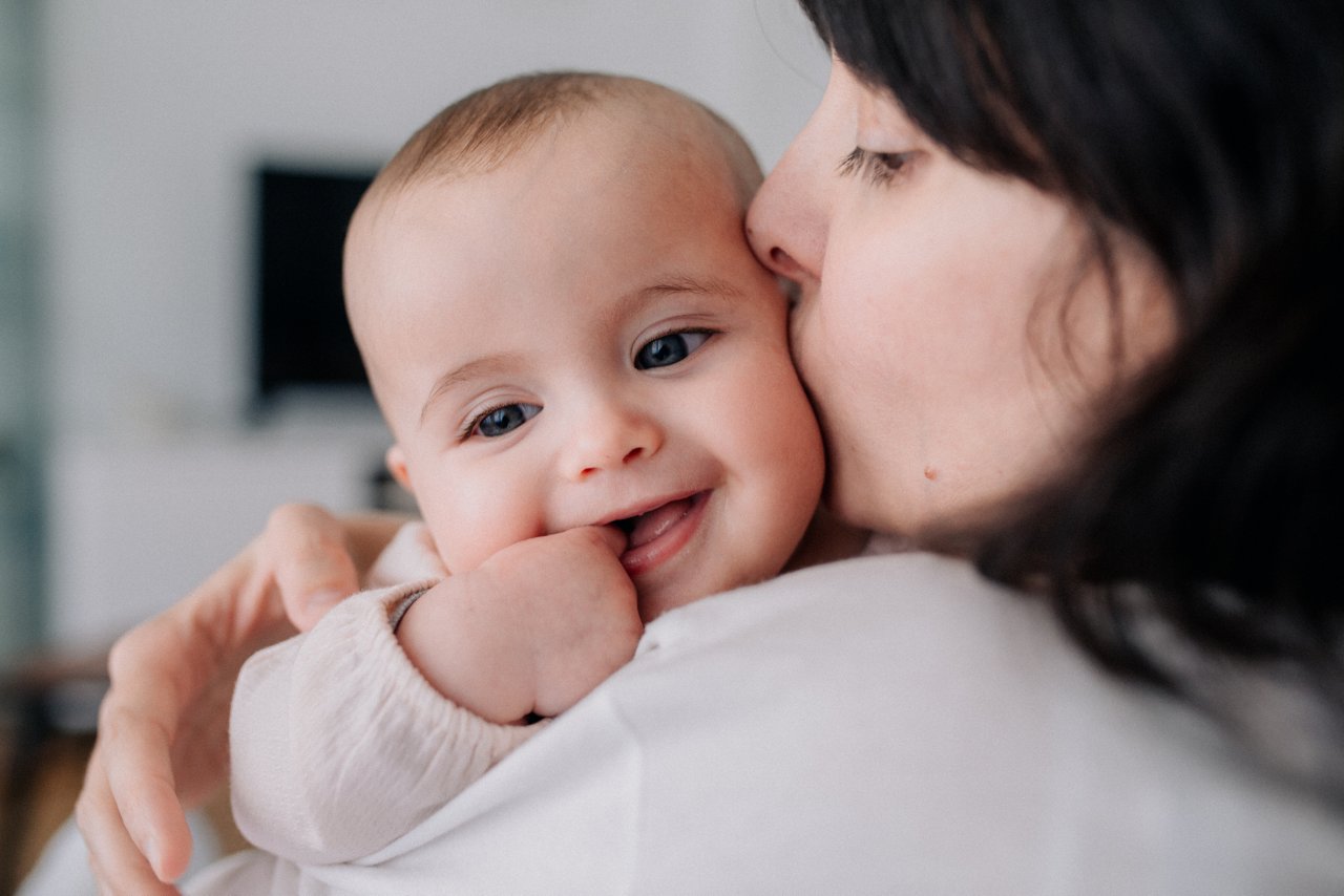 Säugling auf dem Arm der Mutter wird von ihr geküsst und schaut zufrieden