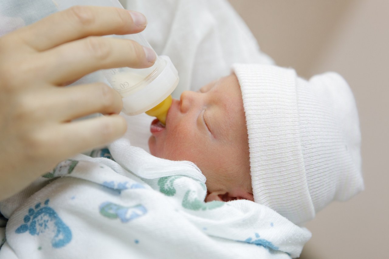 Frühgeborenes mit Mütze wird auf dem Arm mit der Flasche ernährt