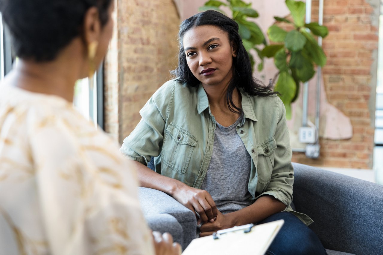 The young adult woman focuses completely on the advice being given by the unrecognizable female therapist.