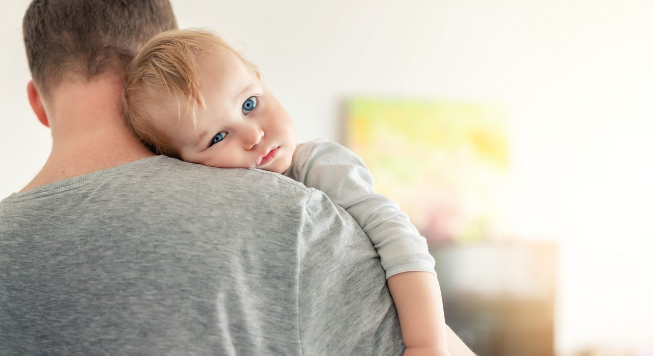 Kleinkind, das aufstoßen und spucken muss, wird auf dem Arm des Vaters getröstet