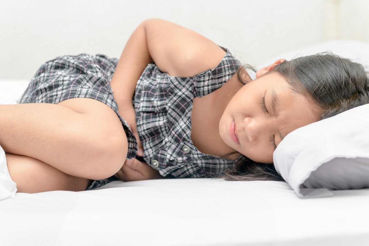 Mädchen mit Bauchschmerzen aufgrund von EGIE liegt im Bett und krümmt sich