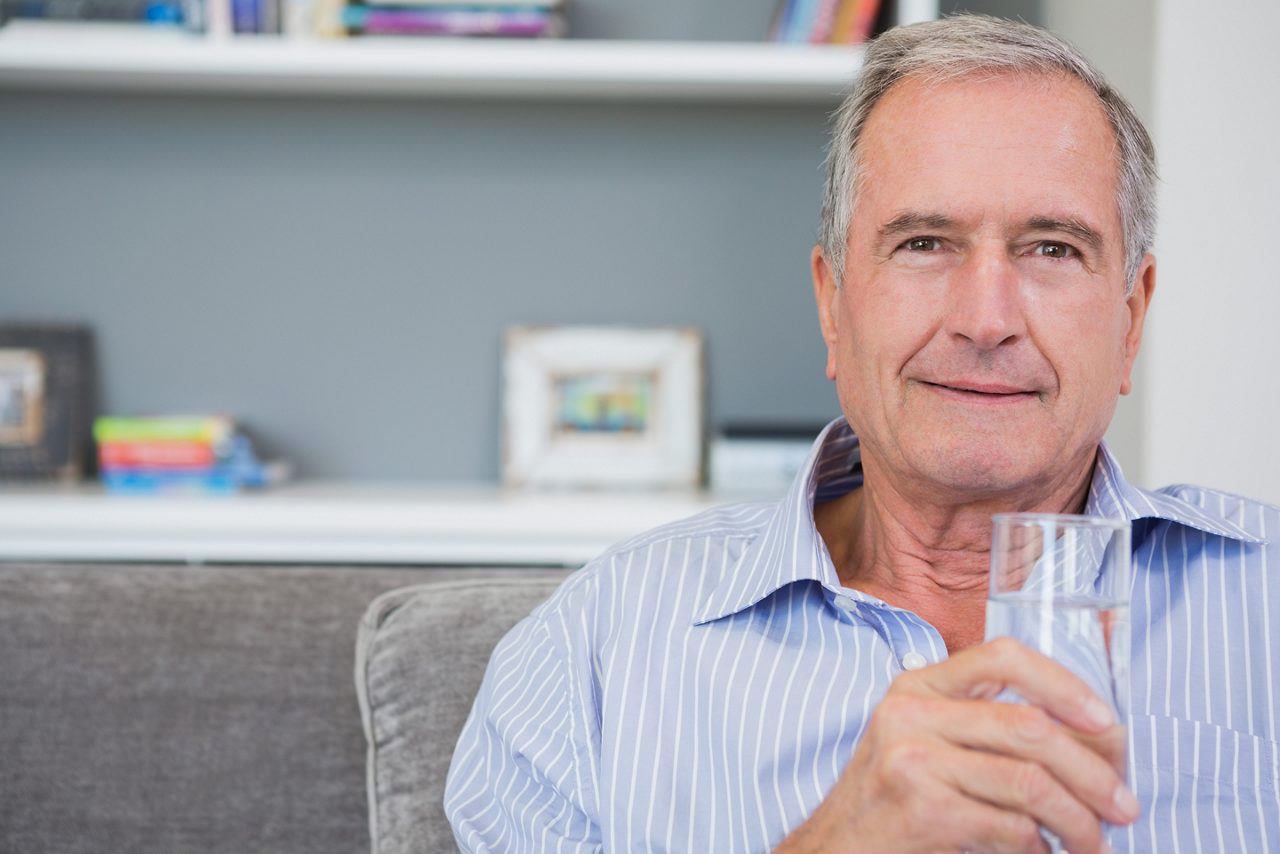 Mann trinkt entspannt aus einem Glas angedickte Flüssigkeit