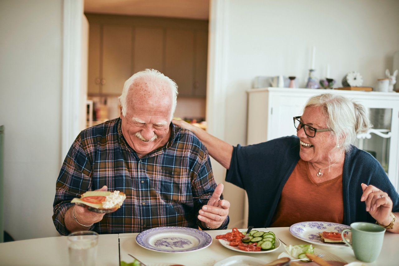 Mann, dem eine Operation bevorsteht, sitzt am Frühstückstisch mit seiner Frau und lacht