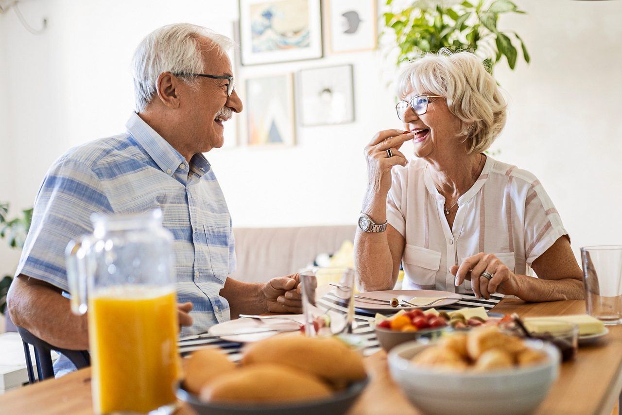 Mann, dem eine Operation bevorsteht, sitzt am Frühstückstisch mit seiner Frau und lacht