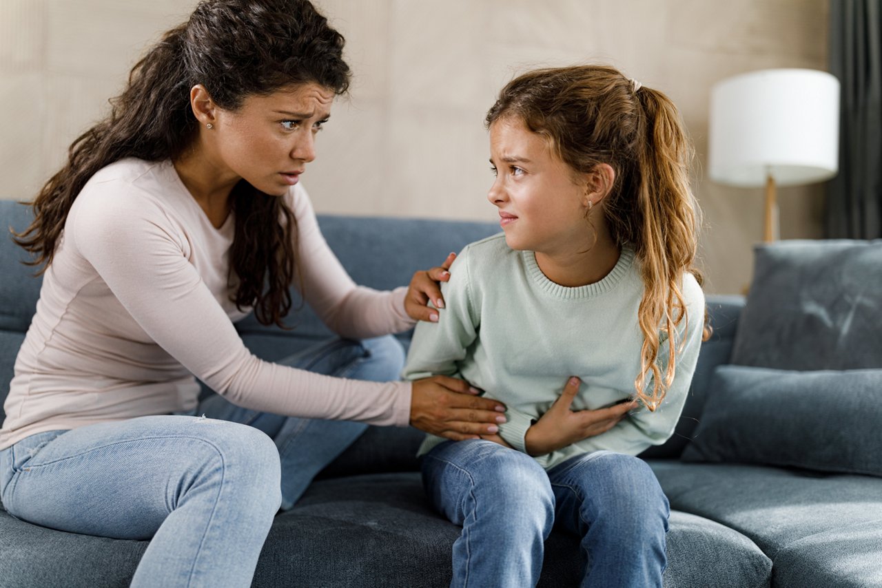 Worried single mother consoling her little girl who is having stomachache at home.