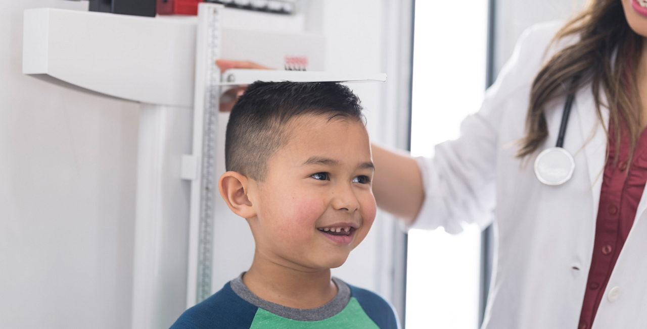 Eine Ärztin misst im Behandlungsraum die Körpergröße eines Jungen mit einer Wandmesslatte.