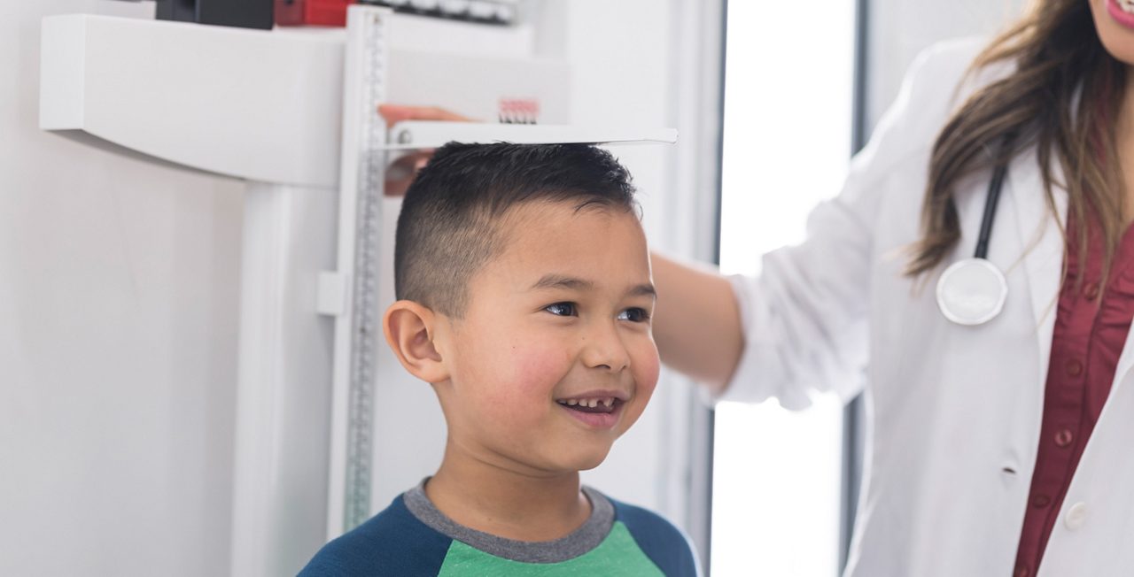 A cute young boy stands on the scale at the doctor's office while the female doctor measures his height.