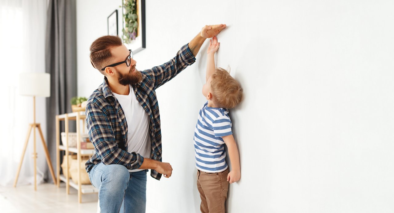 concept of development, growing up. a father measures height of his young child son