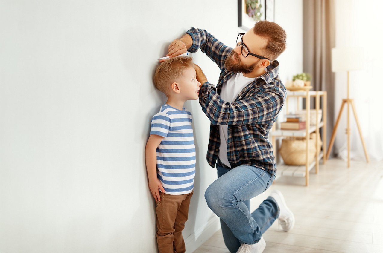 concept of development, growing up. a father measures height of his young child son