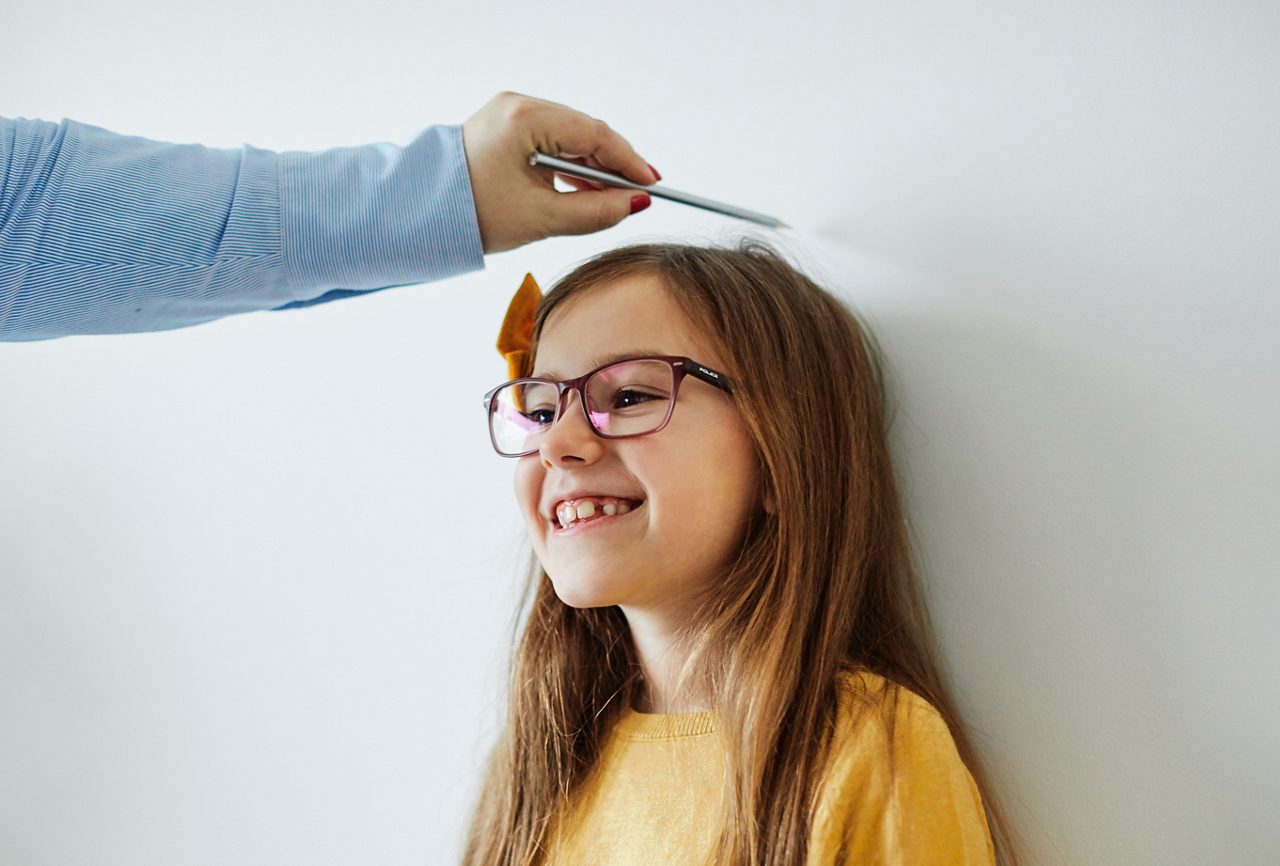 Mother measuring the height of her daughter on the wall at home