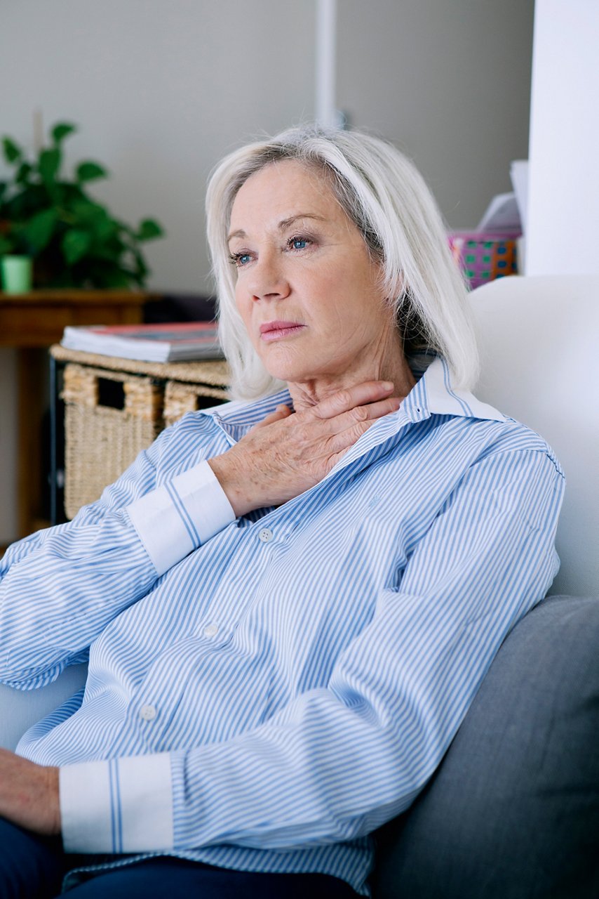 Frau fasst sich mit der Hand an den Hals