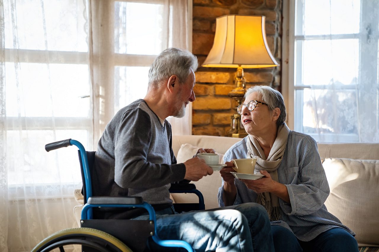 Schlaganfall-Patient im Rollstuhl trinkt Tee mit einer Frau