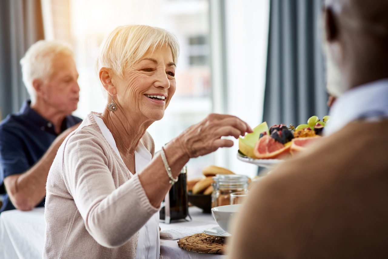 Frau mit Alzheimer-Krankheit in geselliger Runde nimmt sich Obst von einem Teller