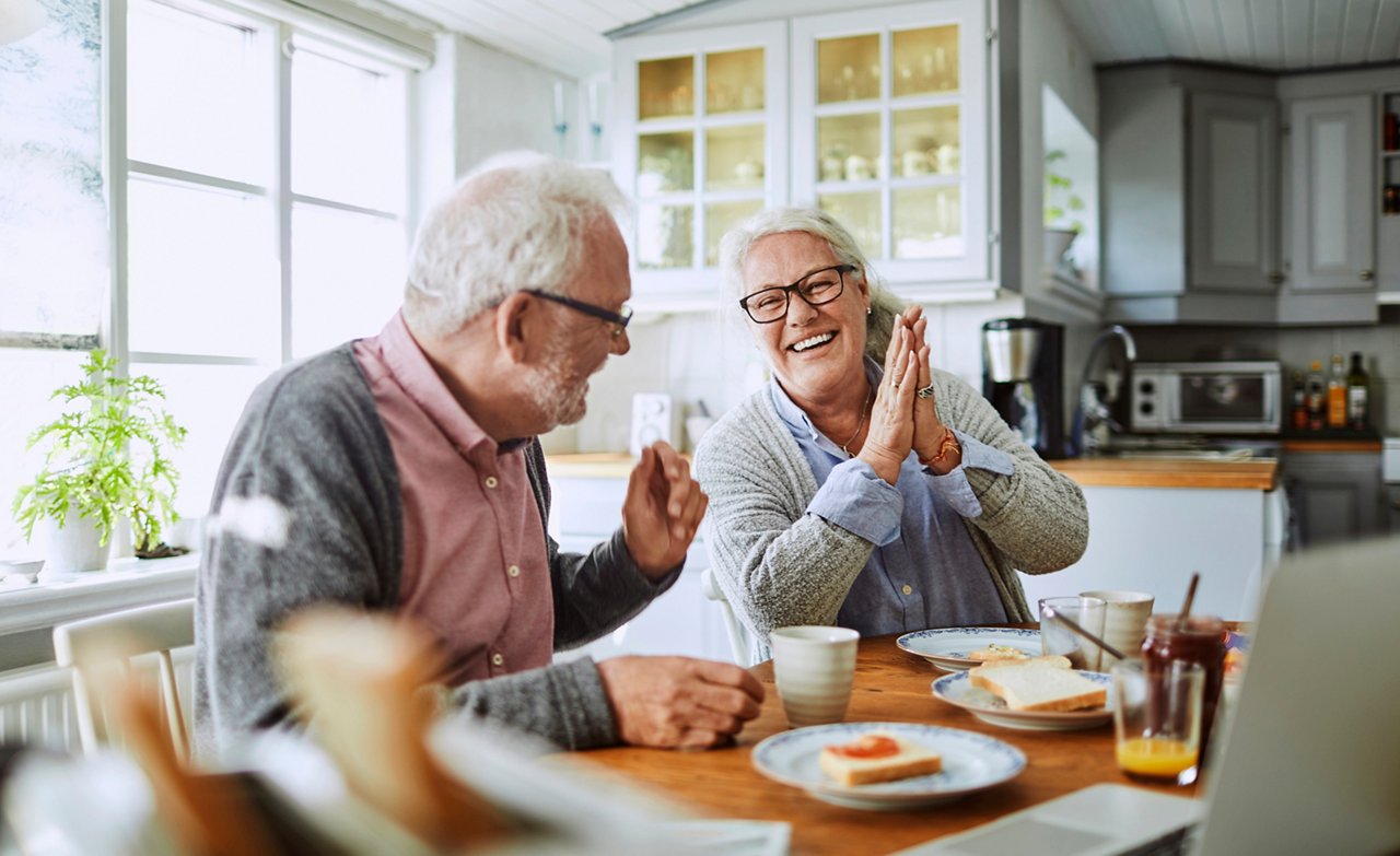 Mann mit Alzheimer-Krankheit sitzt mit seiner Frau am Frühstückstisch und lacht