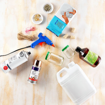 Une collection de fournitures de bricolage disposees sur une surface en bois clair. Les articles comprennent un pistolet a colle bleu, des bocaux en verre, de la ficelle, des bouchons en liege et des bombes de peinture. Le texte visible comprend � 500 ml � sur un recipient blanc et � 500 ml � sur une bouteille a etiquette verte. Le decor suggere des activites de bricolage ou de creation.