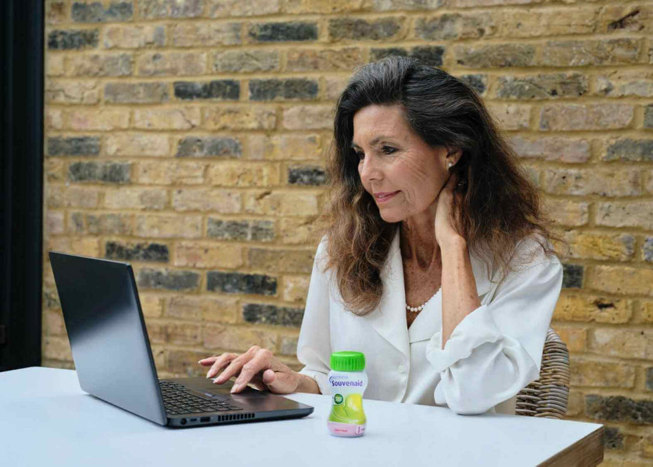 Woman working with laptop and Souvenaid bottle