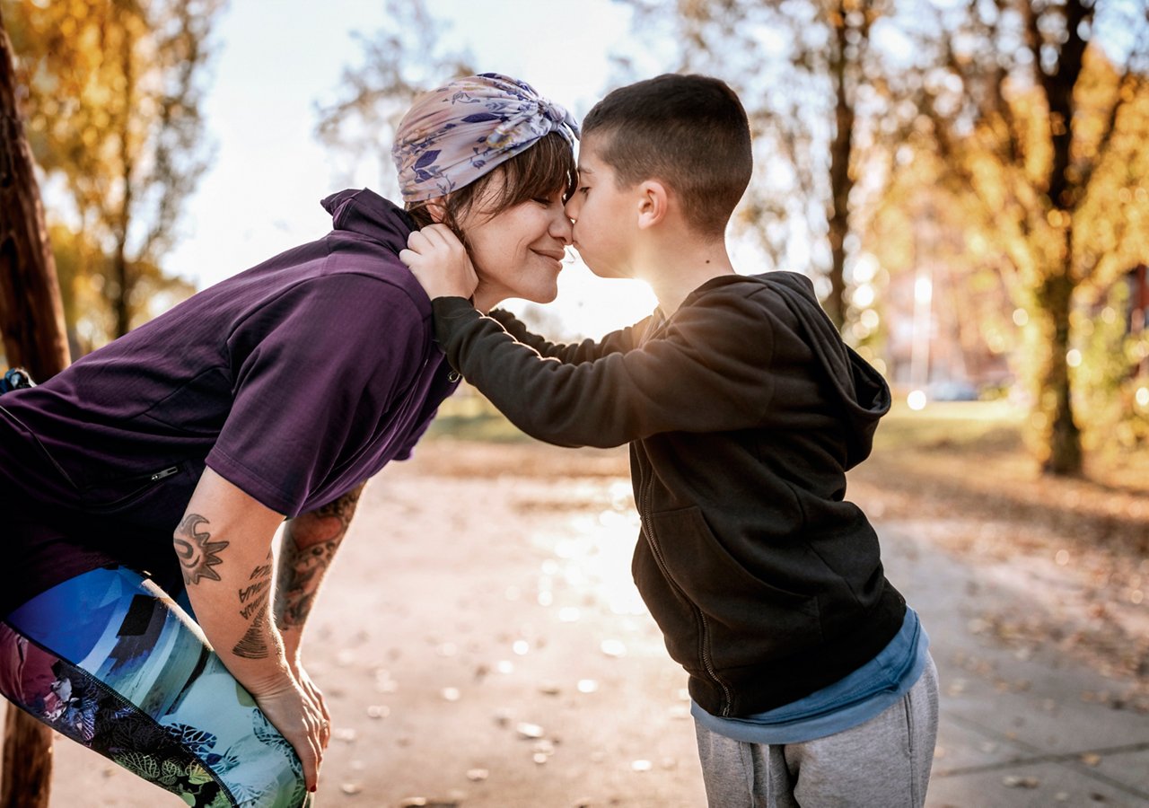 Young woman kissing and embracing her son outdoor, standing face to face on sunny day