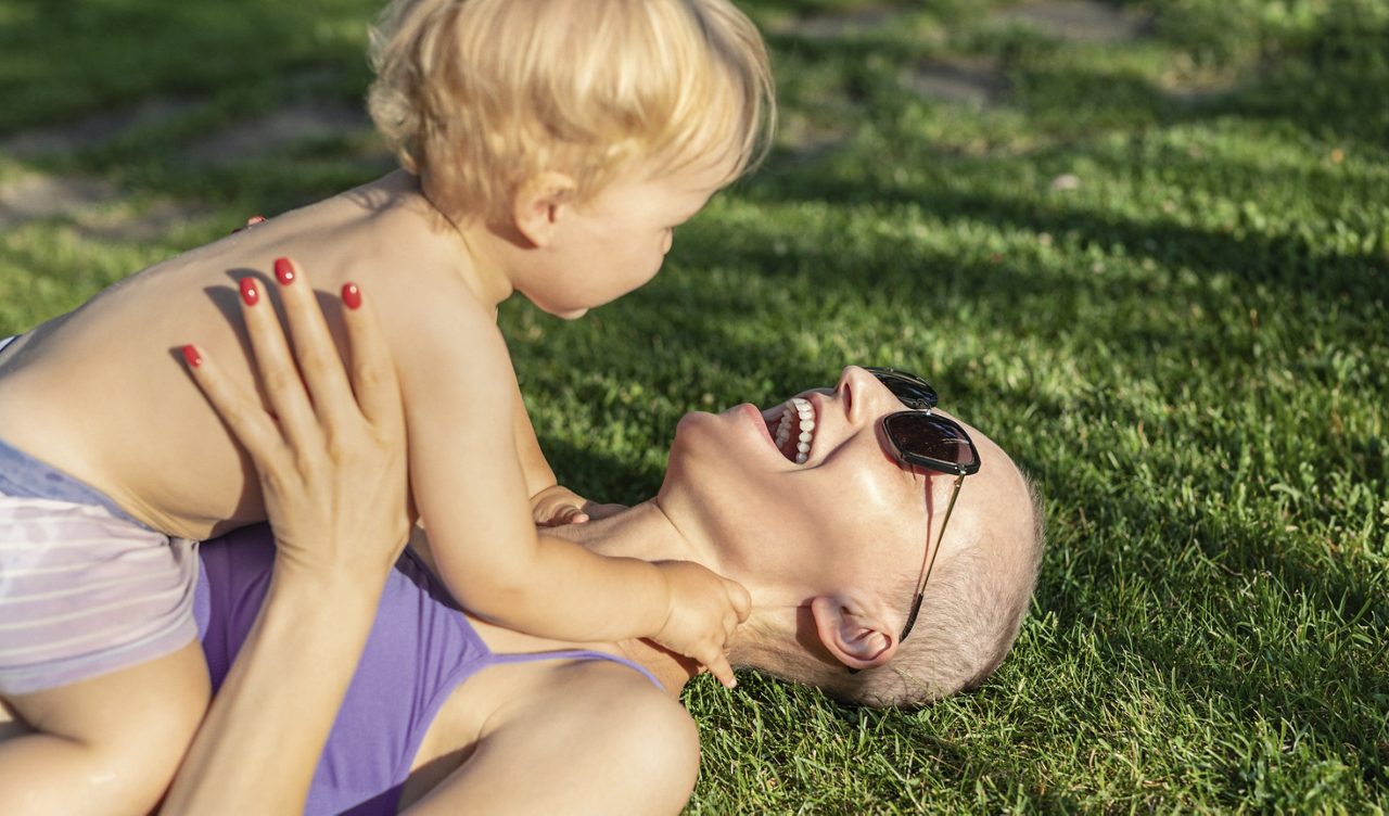Adulte allongé sur l’herbe jouant avec un enfant, moment positif face à la prise en charge de la dénutrition liée au cancer