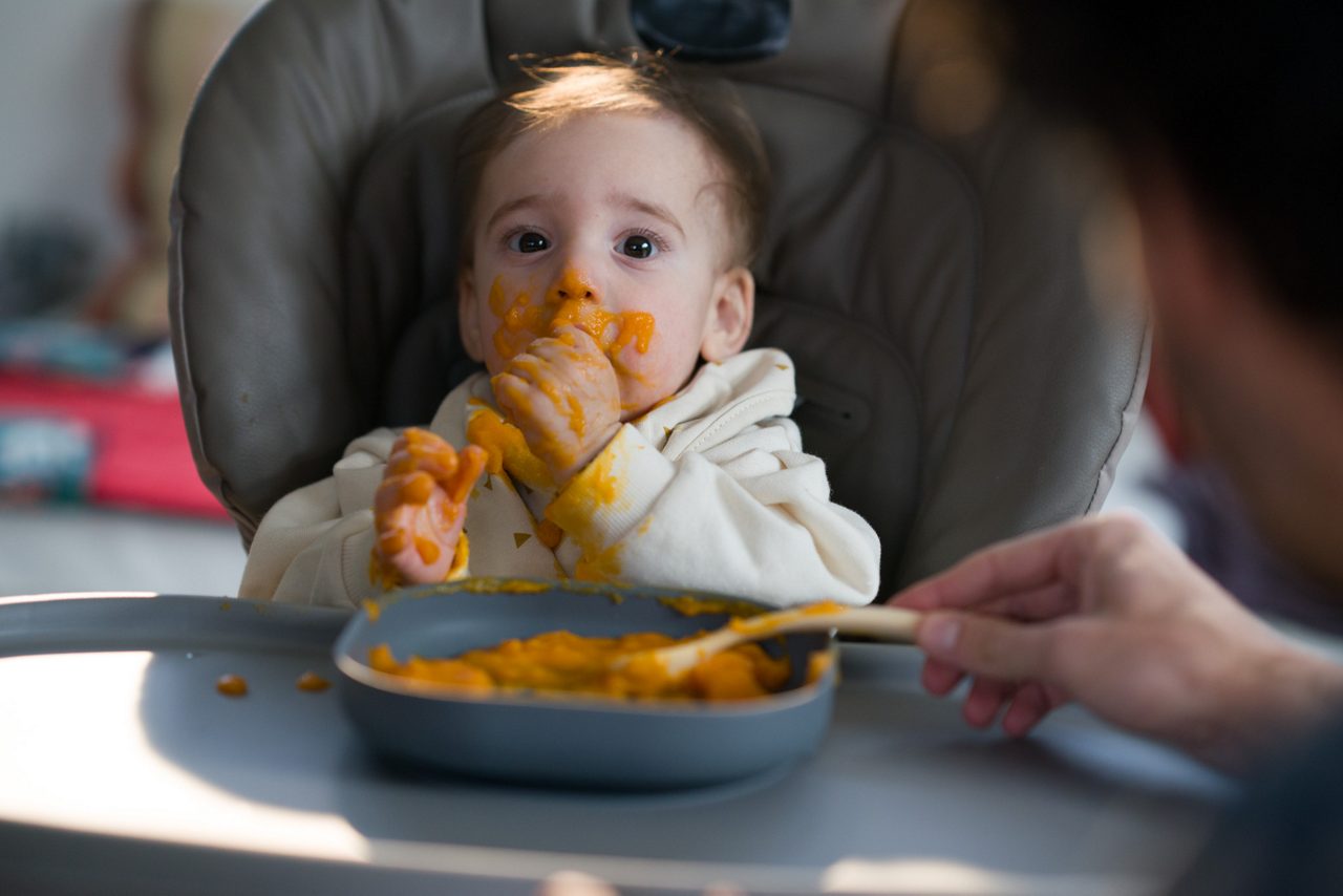 Bébé dans une chaise haute découvrant une purée de légumes lors des premiers repas et de l’apprentissage de nouvelles saveurs.