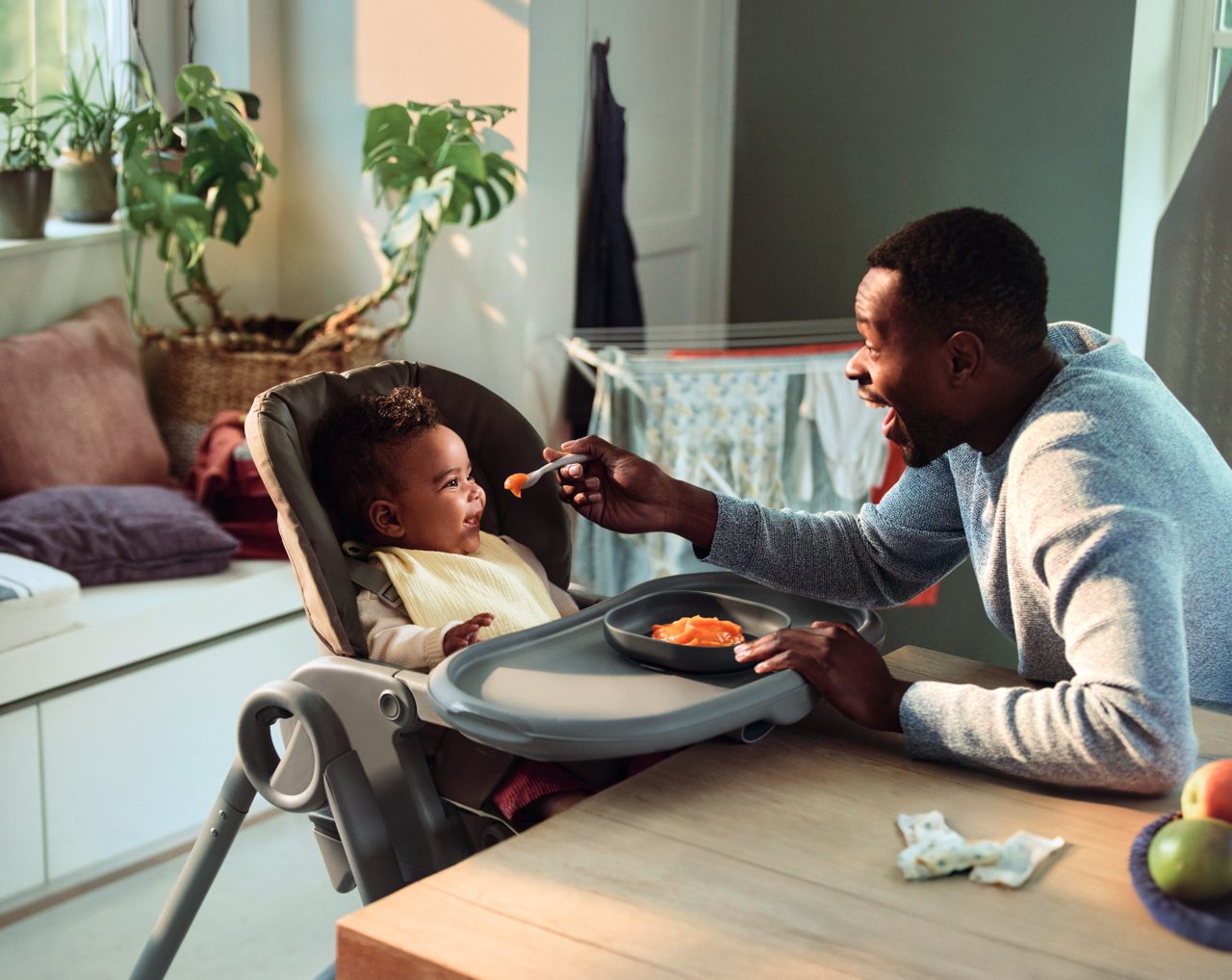 Jeune enfant dans une chaise haute recevant une purée de légumes lors d’un moment familial autour des premiers repas sains.