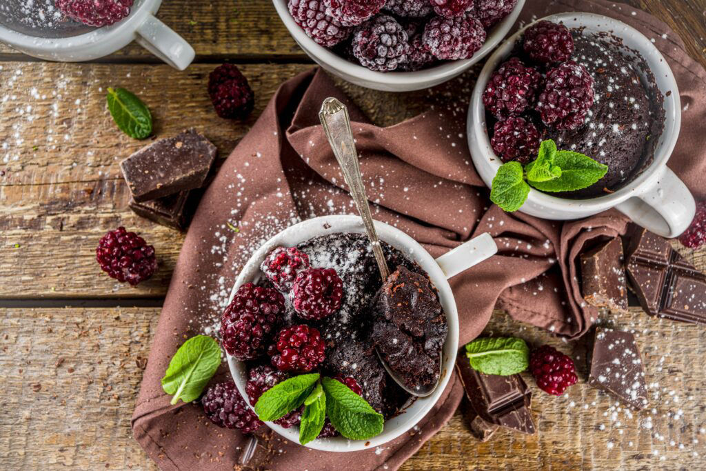 Homemade chocolate mug cake with blackberry. Breakfast easy snack recipe, chocolate non dairy cake in mugs, with blackberry, sugar powder and mint, wooden rustic background