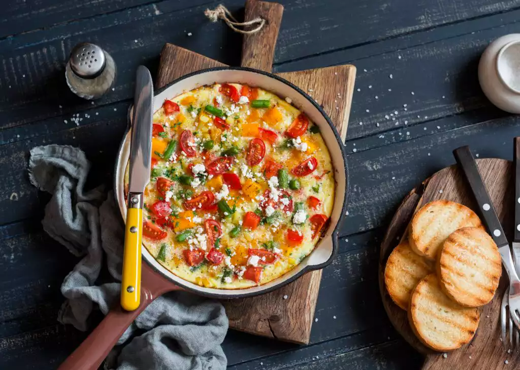 Vegetable frittata in a cast iron skillet on wooden background. Delicious brunch, top view