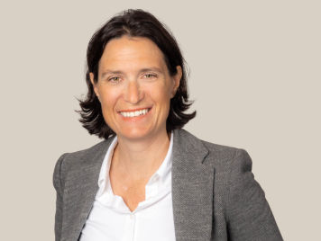 Geraldine Moret, Vice President, Operations at Danone Canada, wears a grey blazer and a confident expression, she smiles. She has short straight hair.