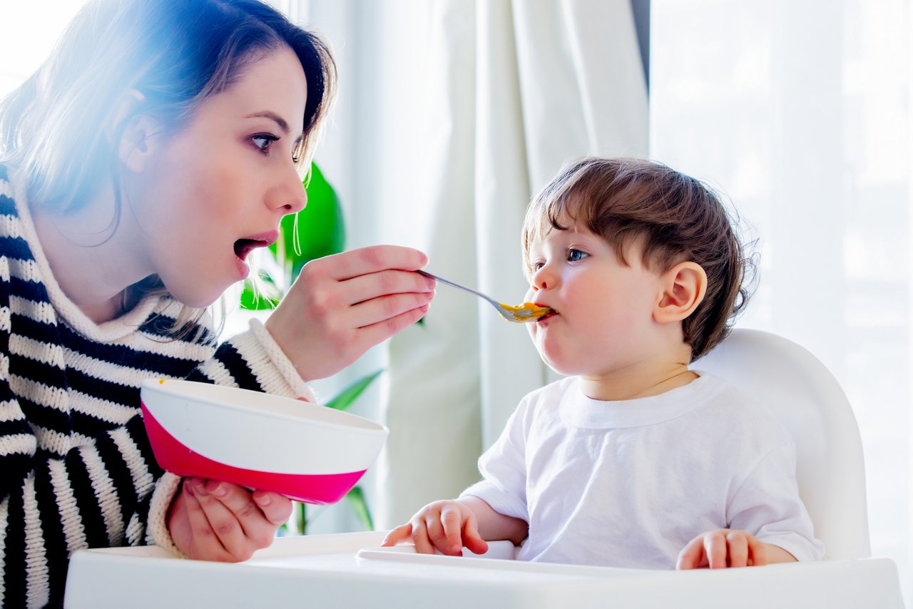 Young mother try to feeding a toddler boy with a spoon in a chair getty images 1146970769