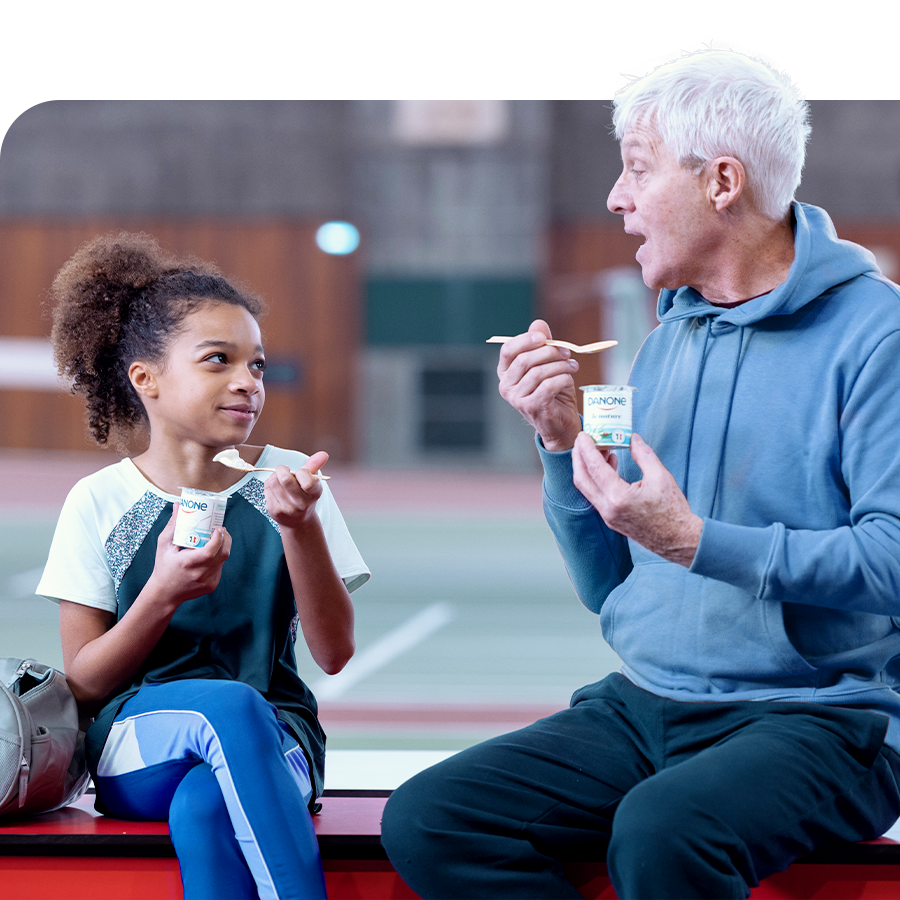 Image of a child and an older man, seating side by side, talking with a Danone yogurt in their hands.