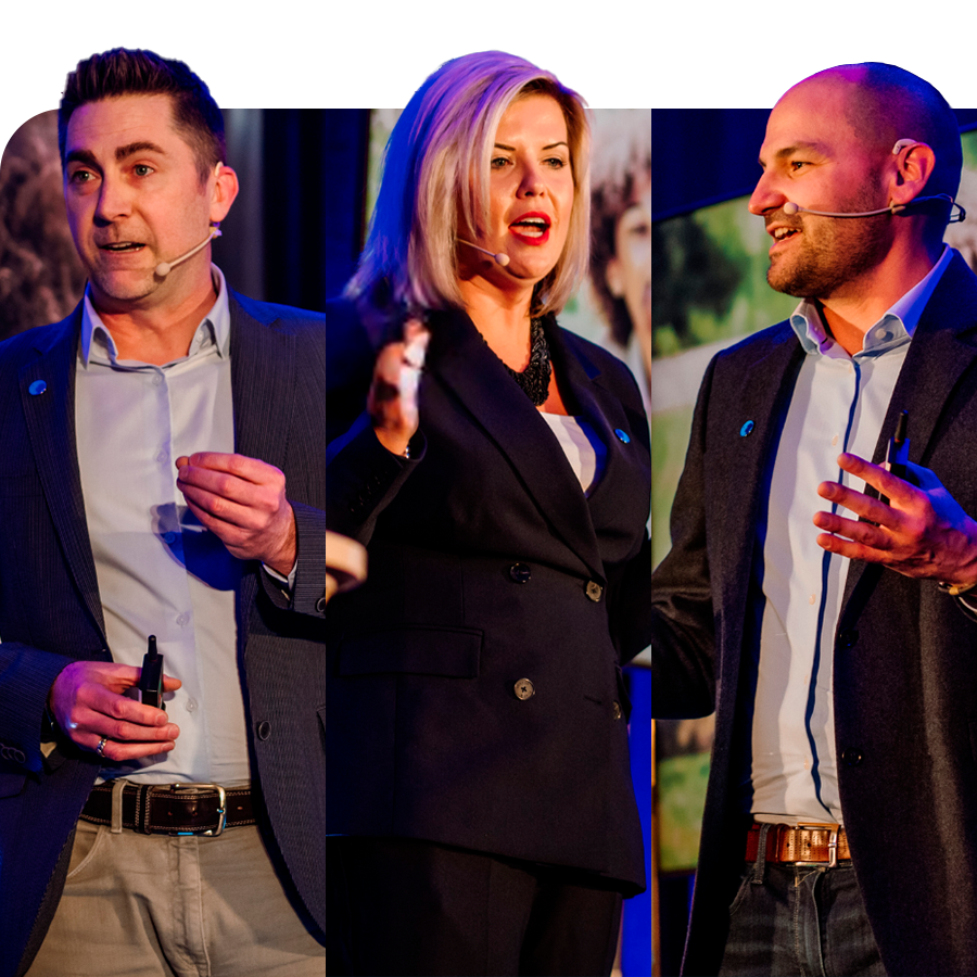 Three Danone Canada leaders stand on stage speaking at an event. From left to right: a man in a blue blazer with short, dark straight hair (Jeremy Oxley), a woman black blazer and blonde hair (Natalie Holloway), and a man with black blazer and a shaved head (Iannick Melancon). They're all wearing a microphone close to their mouth.