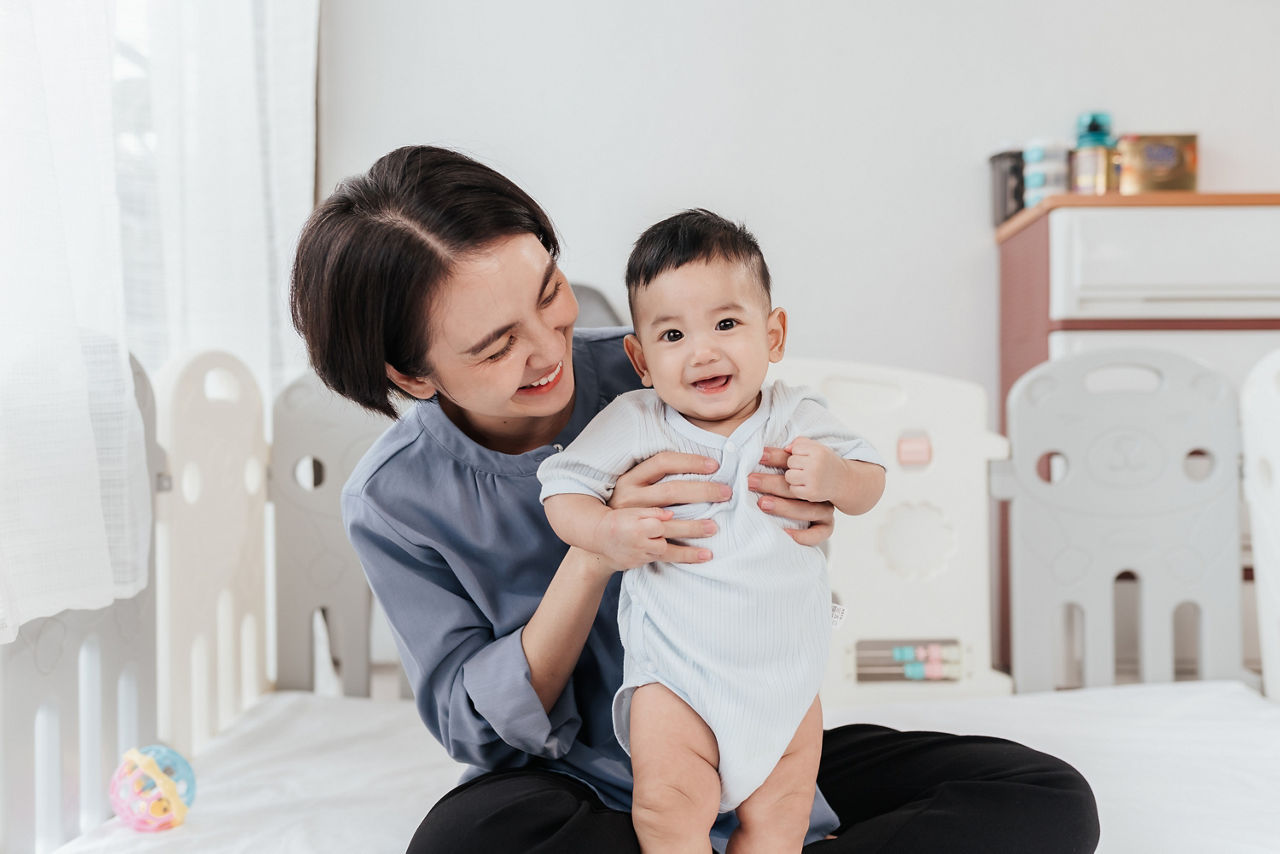 Asian mom lifting and playing newborn baby. Happiness Asian mother conference and playing with adorable her son looking at camera. Happy asian family healthcare love together mother day concept.