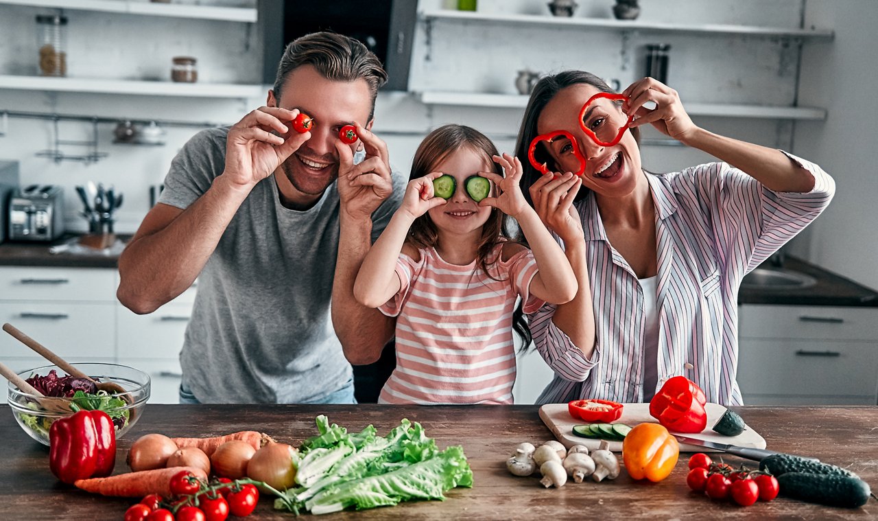 Mom, dad and daughter are cooking on kitchen. Happy family concept. Handsome man, attractive young woman and their cute little daughter are making salad together. Healthy lifestyle.