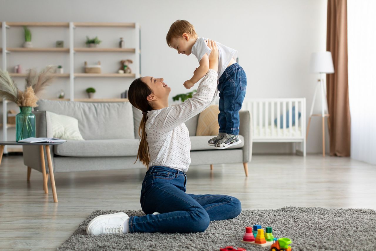 Unconditional love. Happy young mother enjoying time with her adorable toddler son at home, lifting him in the air, playing with kid boy in living room, free space
