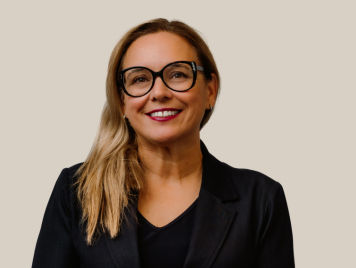 Isabelle Rayle-Doiron, Senior Vice President, General Secretary at Danone Canada, wears a black blazer and a confident expression, her smile accented by bold-framed glasses. She has long straight hair.