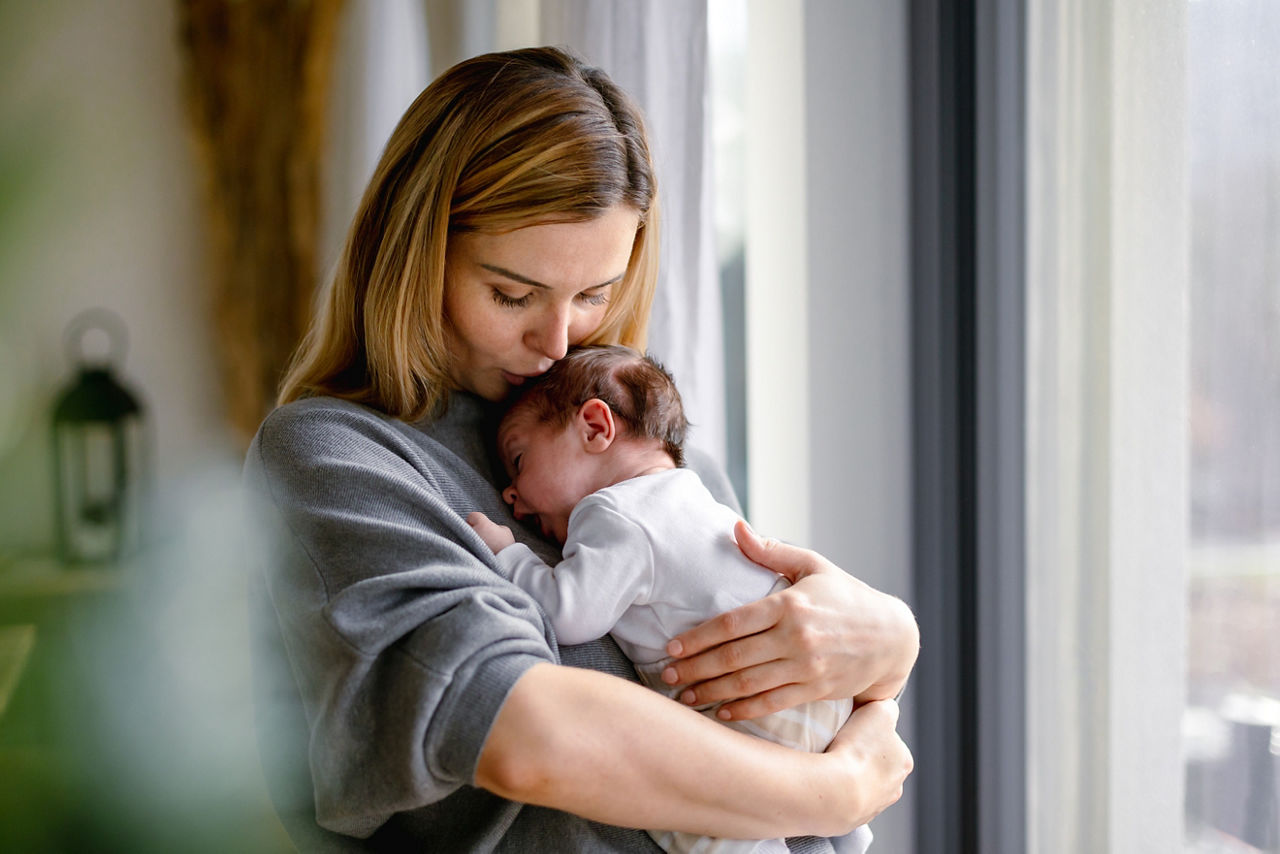 Woman checking temperature of infant formula at table indoors, closeup. Baby milk