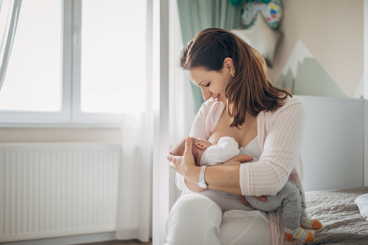 Woman checking temperature of infant formula at table indoors, closeup. Baby milk