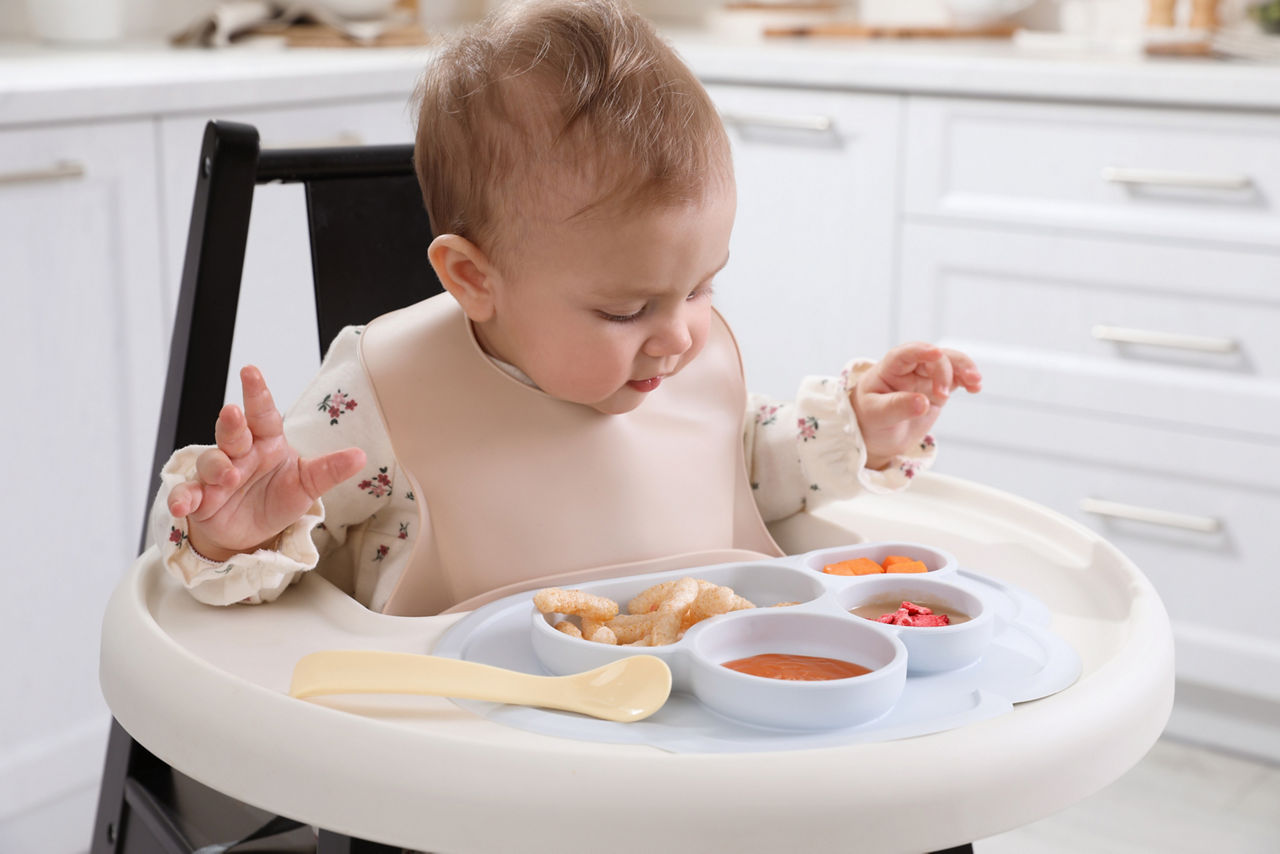 Woman checking temperature of infant formula at table indoors, closeup. Baby milk