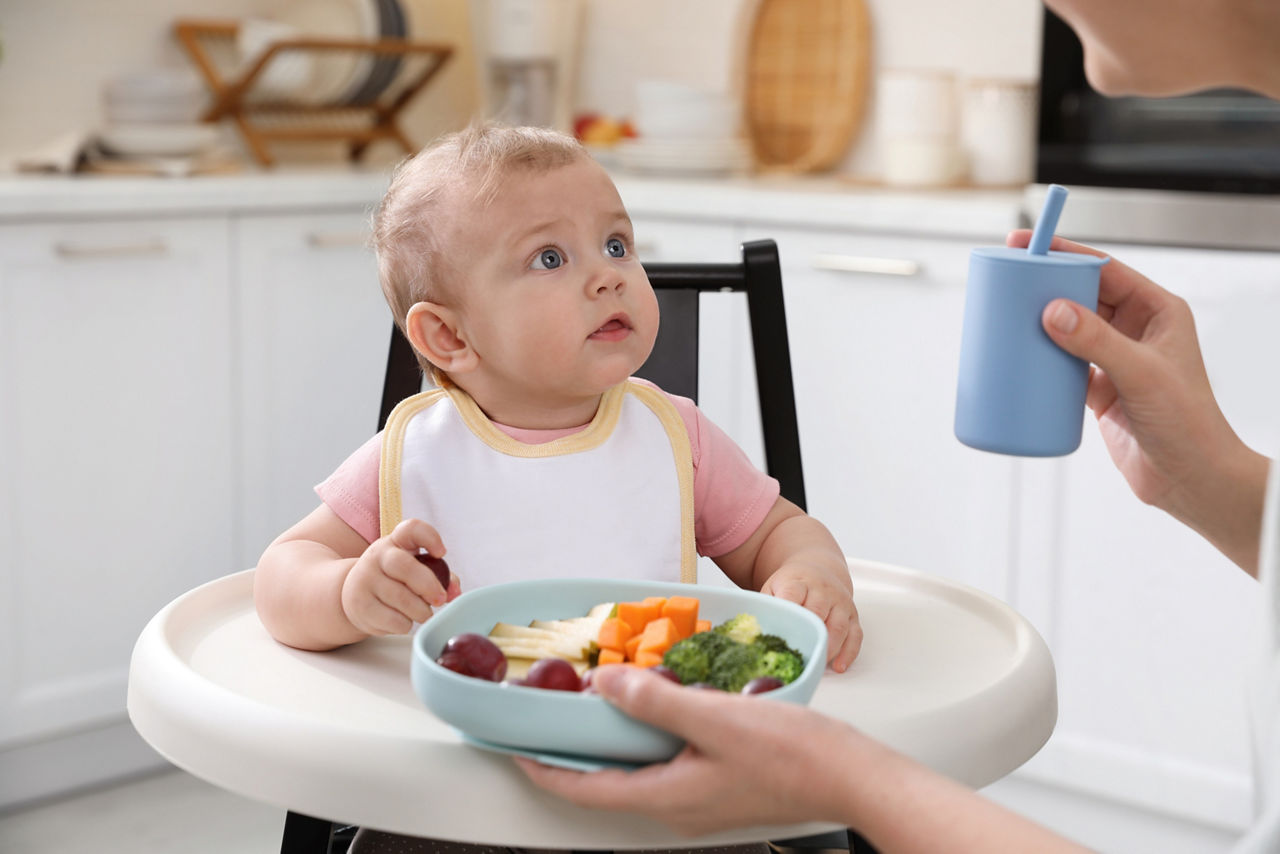 Woman checking temperature of infant formula at table indoors, closeup. Baby milk