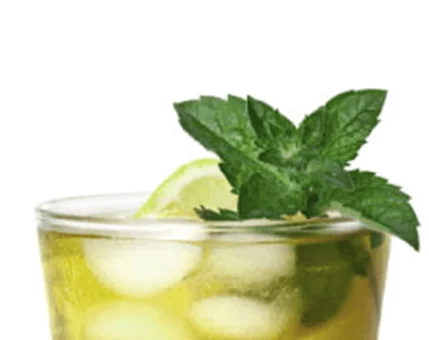 A chilled beverage served in a glass, featuring ice cubes and a vibrant mint garnish. A slice of lime adds a zesty touch to the drink. The golden hue of the liquid suggests a tea or cocktail base, perfect for a refreshing moment.