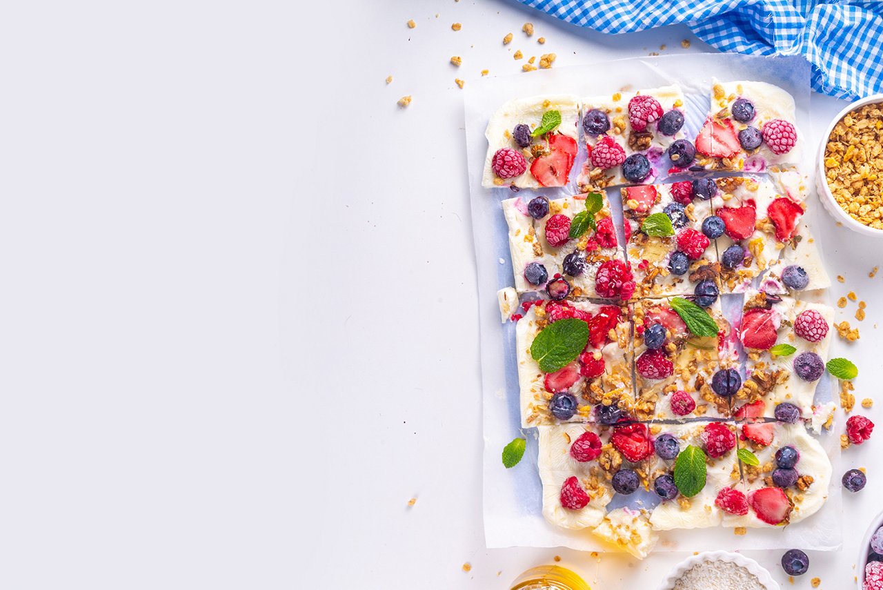 Homemade frozen Yogurt Bark, alternative healthy keto diet ice cream made from greek yogurt, fresh berries, nuts, granola, honey, on baking tray deco. Frozen yoghurt bars with fruit berry toppings