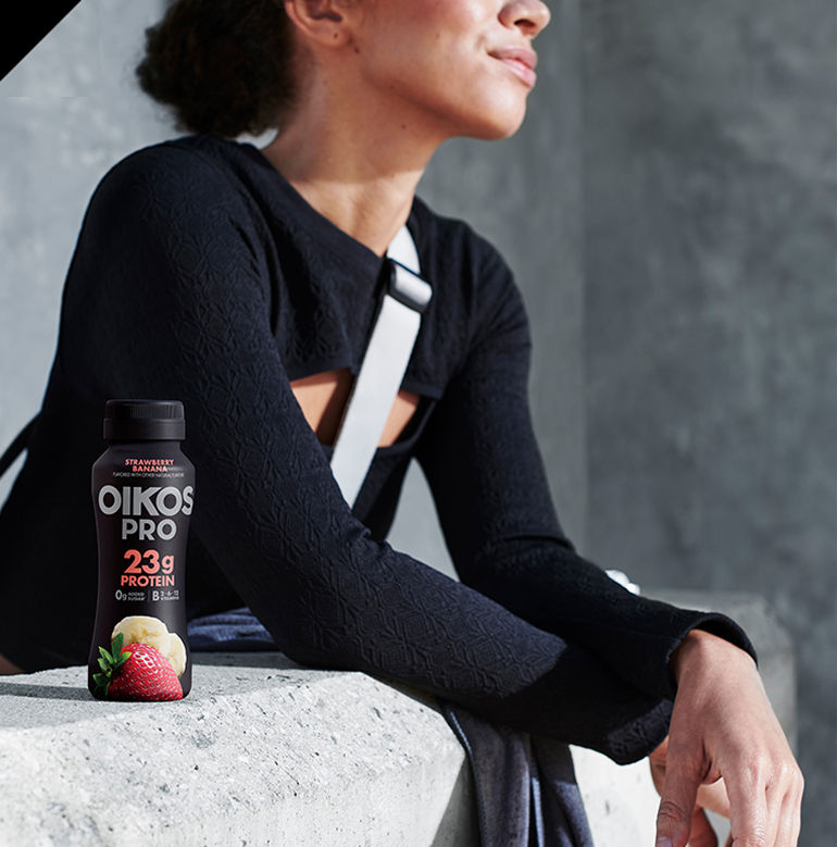 Woman resting her arms on a concrete and a OIkos strawberry banana 