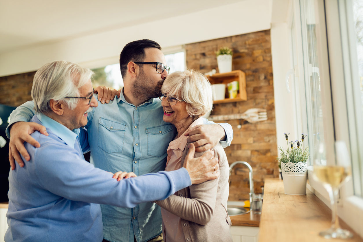Happy mature couple embracing their adult son while greeting with him in the kitchen.