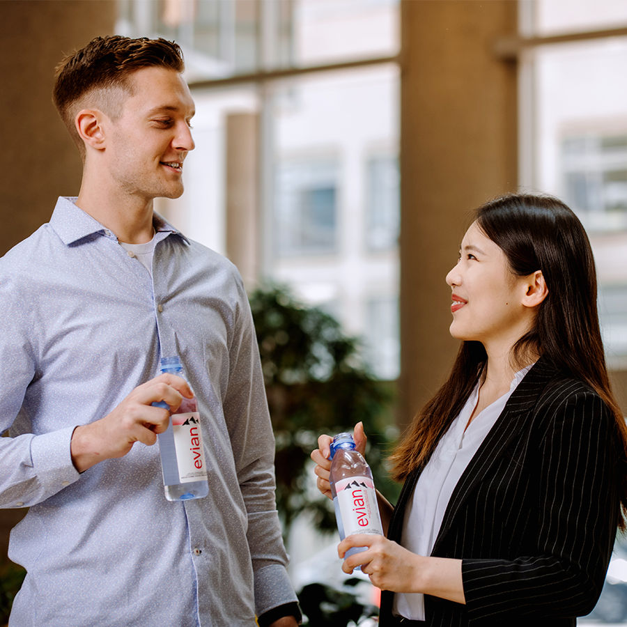 Two colleagues engage in a friendly conversation while holding bottles of evian water.