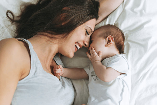Mamá sonriente acostada junto a un bebé con las cabezas encontradas