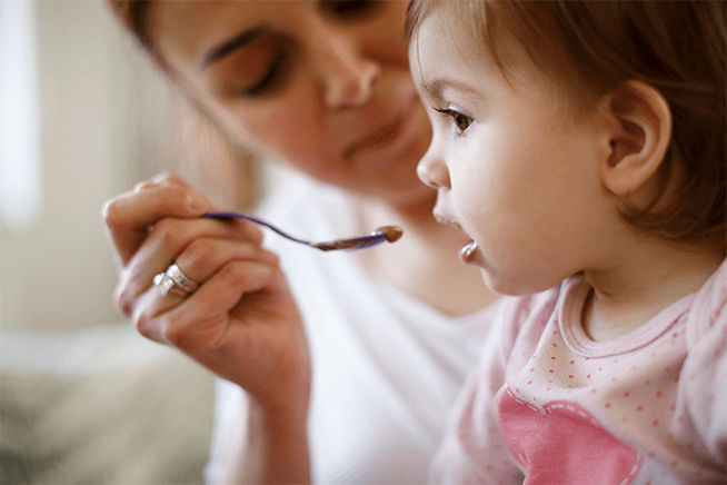 Primer plano de una mamá alimentando con cuchara a una bebé