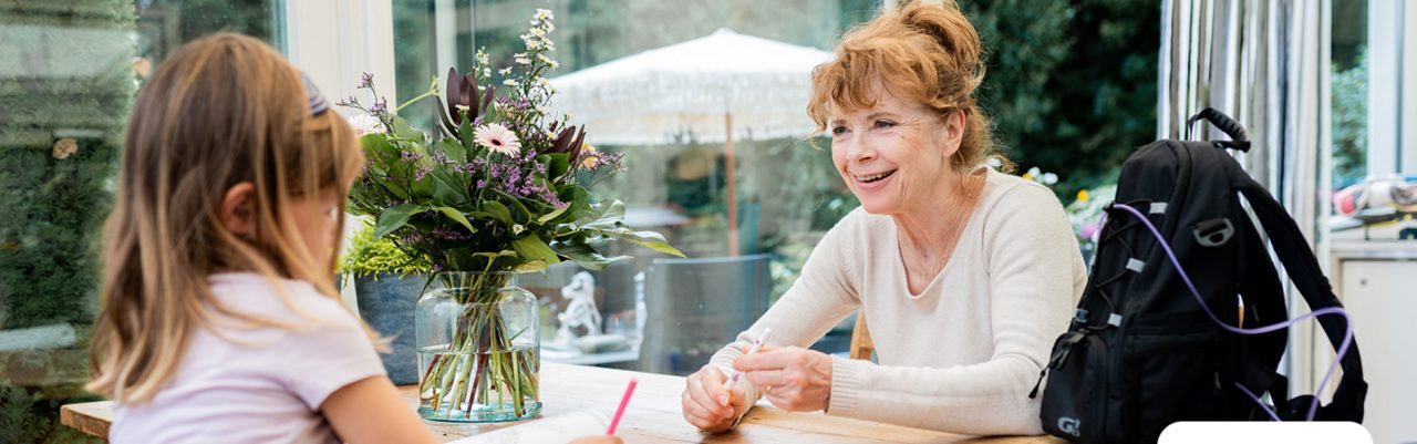 Persoon met draagbare voedingspomp in gesprek met een kind aan de keukentafel, illustratie van sondevoeding thuis en dagelijks leven met medische voeding.