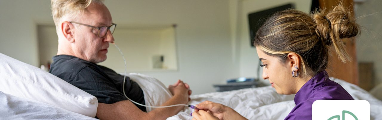 Persoon ontvangt sondevoeding via een neus-maagsonde met ondersteuning van een zorgverlener thuis.