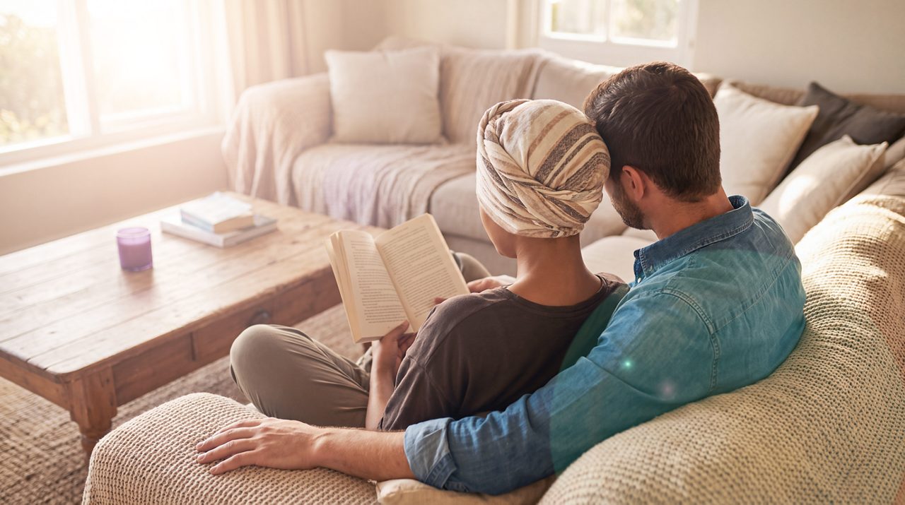 AI generated image of female cancer patient and male partner reading on sofa.