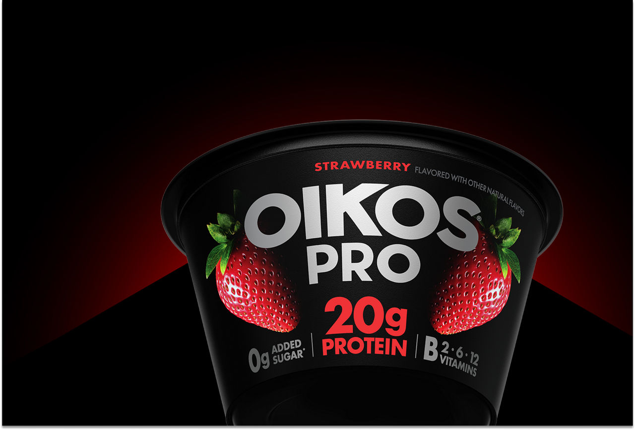 A cup of the rennovated Oikos Pro strawberry cup highlighted by a red light in the background.